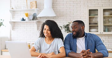 man and woman looking at computer at kitchen table