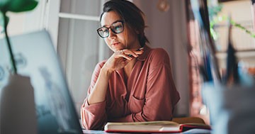 woman holding pen looking at computer screen