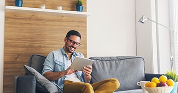 man sitting on couch smiling while looking at tablet