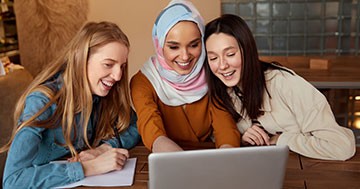 three friends sitting around computer in coffee shop