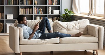 man lying on couch while looking at cellphone