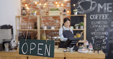 woman at counter of small business with open sign in window